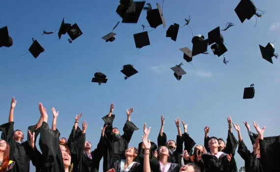 newly graduated people wearing black academy gowns throwing hats up in the air